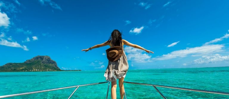 Een vrouw spreid haar armen op de boeg van een schip in de wateren rond Mauritius